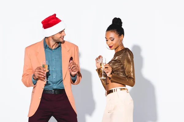 Beautiful african american girl holding champagne glass near smiling man in santa hat on white — Stock Photo