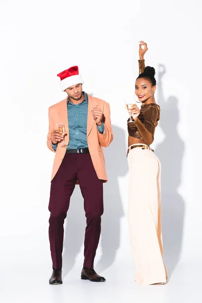 Schöne afrikanisch-amerikanische Mädchen mit Champagnerglas und Blick in die Kamera in der Nähe Mann mit Weihnachtsmann auf weiß — Stockfoto