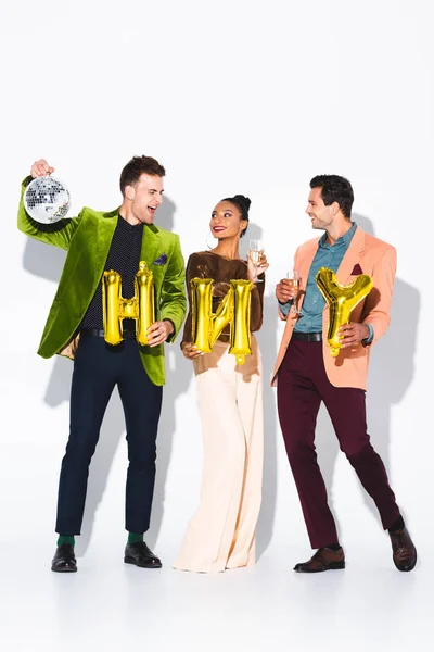 Cheerful african american girl near men, disco ball and balloons on white — Stock Photo