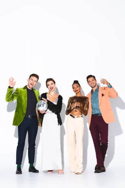 Happy multicultural friends holding champagne glasses and disco ball on white — Stock Photo