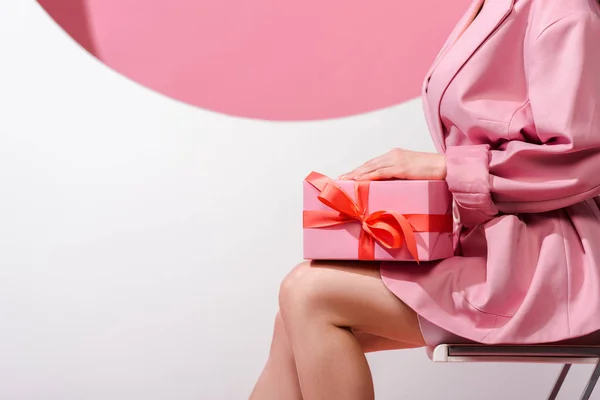 Cropped view of woman sitting on chair and holding present on white and pink — Stock Photo