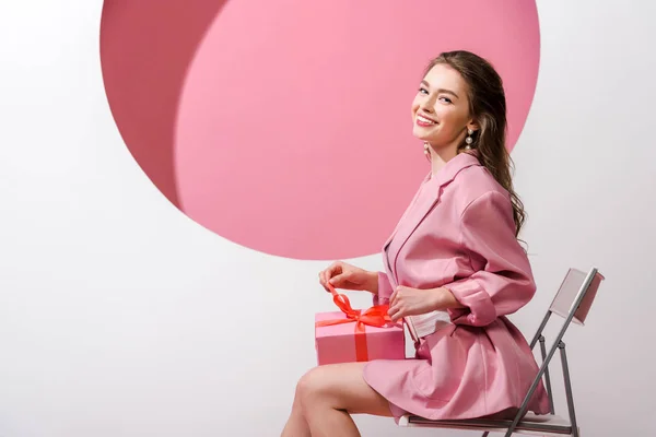 Felice donna seduta sulla sedia e tenuta presente su bianco e rosa — Foto stock