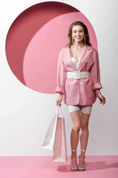 Ragazza allegra ed elegante che tiene borse della spesa su bianco e rosa — Foto stock