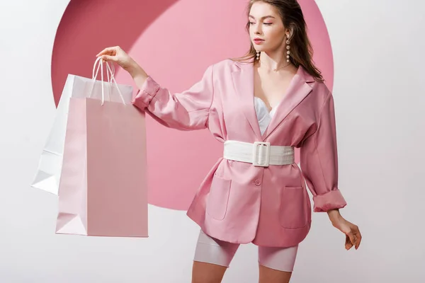 Beautiful girl looking at shopping bags on white and pink — Stock Photo