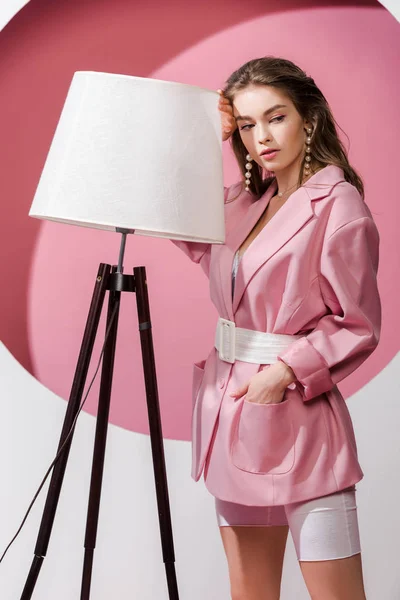 Beautiful girl standing with hand in pocket near floor lamp on white and pink — Stock Photo