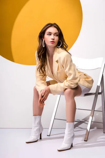 Schönes Mädchen sitzt auf Stuhl auf weiß und orange — Stockfoto
