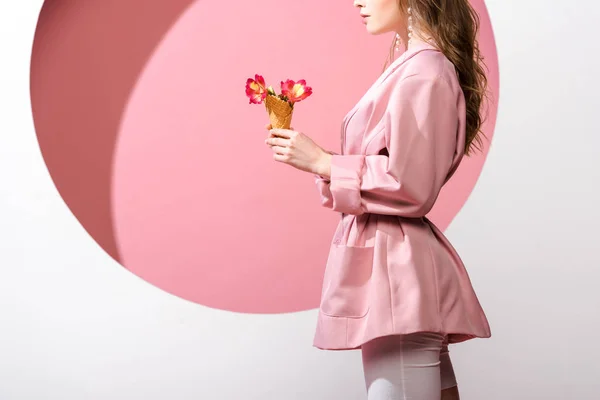 Vista ritagliata di donna che tiene cono gelato con fiori su bianco e rosa — Foto stock