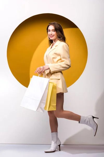 Felice ragazza in piedi con le borse della spesa su bianco e arancione — Foto stock