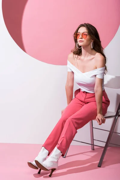 Attraktives Mädchen mit Sonnenbrille sitzt auf Stuhl auf weiß und rosa — Stockfoto