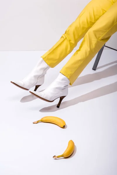 Vista cortada de mulher em botas perto de bananas em branco — Fotografia de Stock