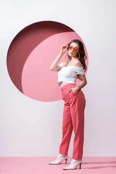 Beautiful girl touching sunglasses on white and pink — Stock Photo