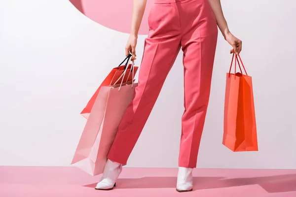 Cropped view of woman holding shopping bags on pink and white — Stock Photo