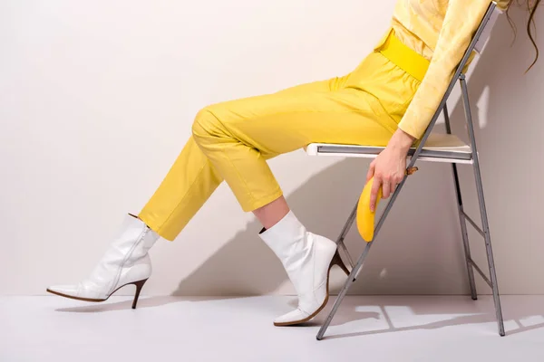 Vista recortada de la mujer sentada en la silla y sosteniendo plátano amarillo en blanco - foto de stock