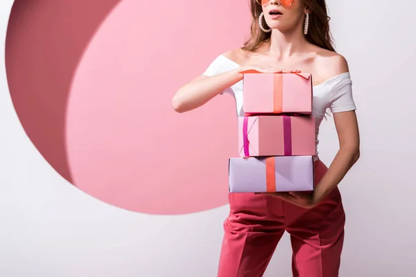 Vista recortada de la mujer sorprendida sosteniendo regalos en rosa y blanco - foto de stock