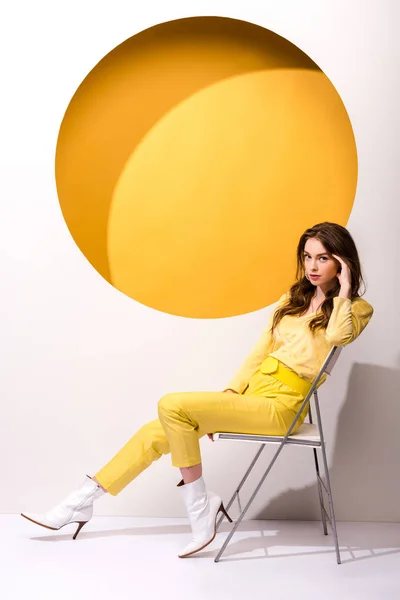 Стильна дівчина сидить на стільці на помаранчевому і білому — стокове фото