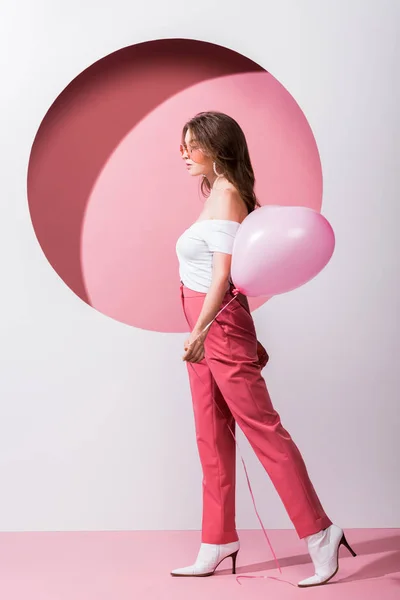 Side view of attractive woman holding balloon on pink and white — Stock Photo