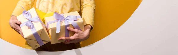 Panoramic shot of woman holding gifts on orange and white — Stock Photo