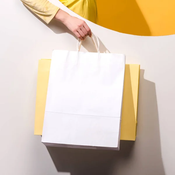 Vue recadrée de la femme tenant des sacs à provisions sur orange et blanc — Photo de stock