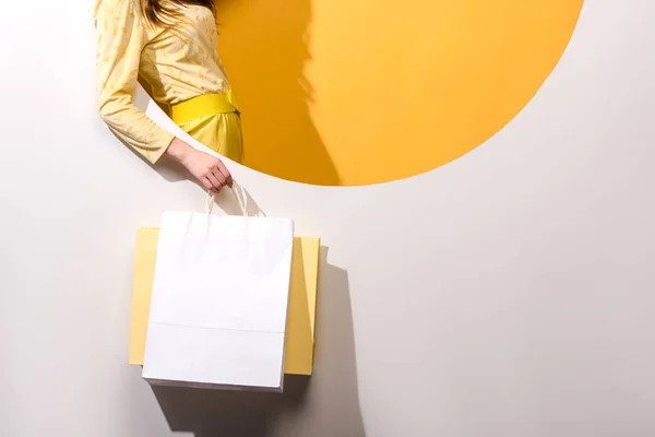 Cropped view of young woman holding shopping bags on orange and white — Stock Photo