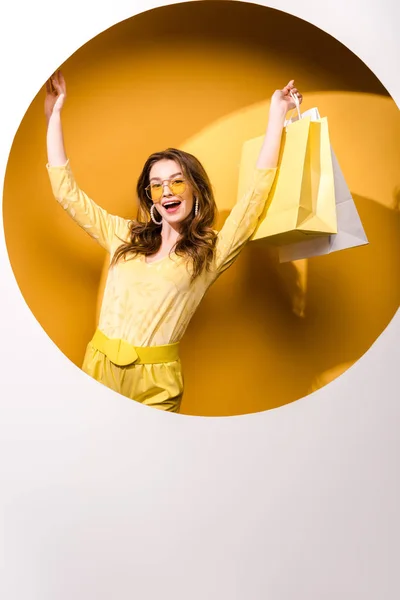 Femme heureuse dans des lunettes de soleil tenant des sacs à provisions sur orange et blanc — Photo de stock