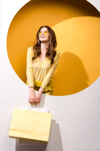 Mulher sorridente em óculos de sol segurando sacos de compras em laranja e branco — Fotografia de Stock