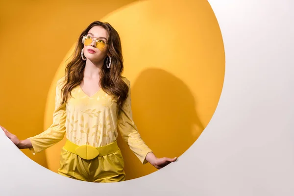 Belle femme en lunettes de soleil debout et regardant loin sur orange et blanc — Photo de stock