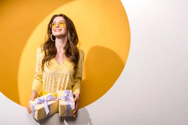 Весела жінка в сонцезахисних окулярах тримає подарунки на помаранчевому та білому — стокове фото