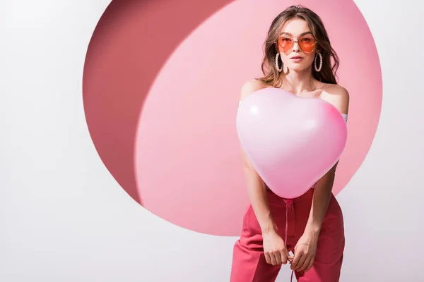 Молодая привлекательная женщина держит воздушный шар на розовом и белом — стоковое фото