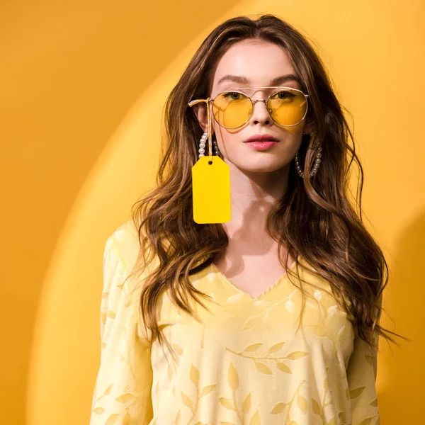 Mujer atractiva en gafas de sol con etiqueta de precio en blanco en amarillo y naranja — Stock Photo