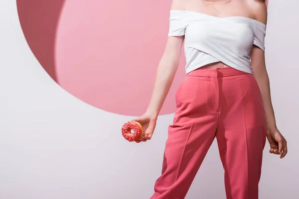 Cropped view of woman holding donghnut on pink and white — стоковое фото