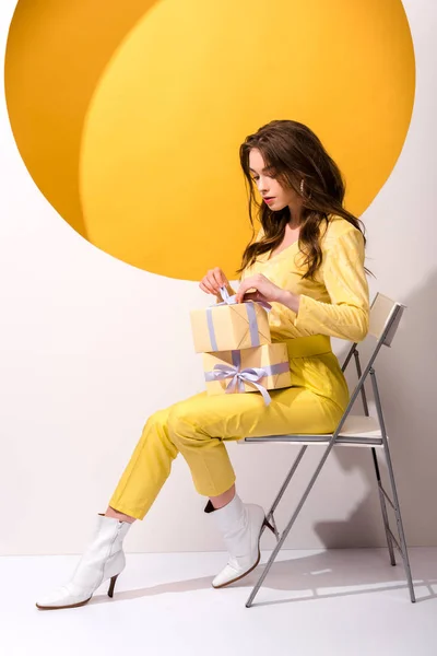 Attractive woman sitting on chair with presents on orange and white — Stock Photo