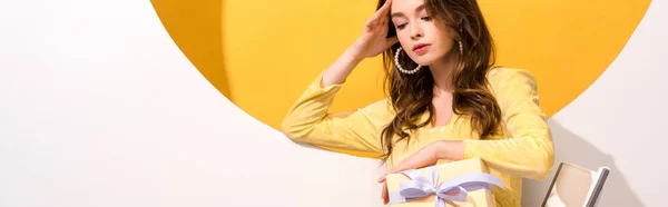 Plano panorámico de mujer atractiva mirando regalos en naranja y blanco - foto de stock