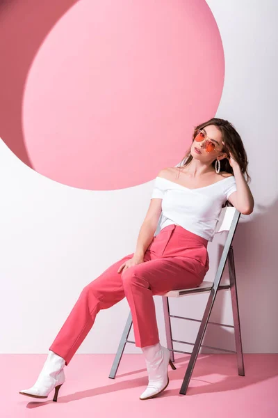 Стильна жінка сидить на стільці на рожевому і білому — стокове фото