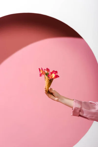 Cropped view of young woman holding ice cream cone with flowers on pink and white — Stock Photo