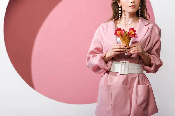 Cropped view of woman holding ice cream cone with flowers on pink and white — Stock Photo
