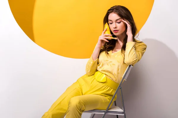 Jovem mulher sentada na cadeira e segurando banana em branco e laranja — Fotografia de Stock