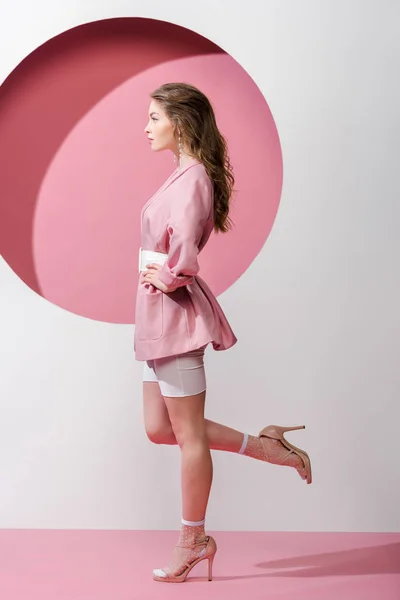 Vue latérale de la femme debout avec la main sur la hanche sur rose et blanc — Photo de stock