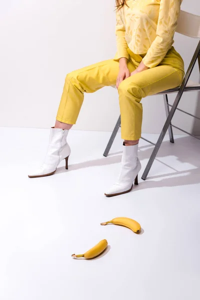 Cropped view of woman sitting near yellow bananas on white — Stock Photo
