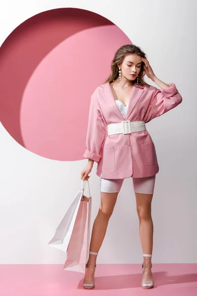 Atractiva mujer joven sosteniendo bolsas de compras en blanco y rosa - foto de stock