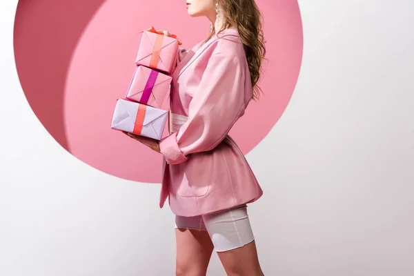 Cropped view of woman holding gifts on pink and white — Stock Photo