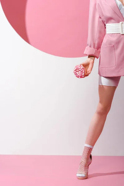 Cropped view of woman standing and holding sweet doughnut on pink and white — Stock Photo