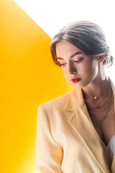 Beautiful young woman in necklace and earrings on orange and white — Stock Photo