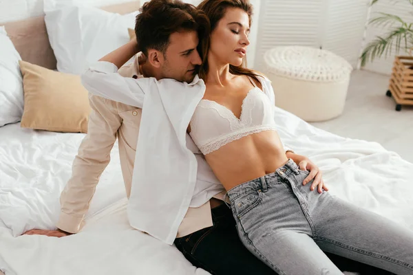 Girlfriend in bra hugging and sitting on boyfriend in apartment — Stock Photo