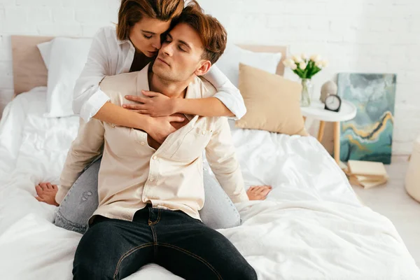 Attractive girlfriend with closed eyes hugging and kissing handsome boyfriend in apartment — Stock Photo