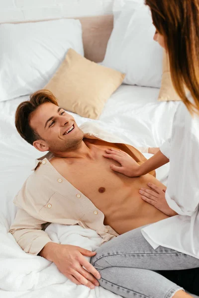 Cropped view of girlfriend hugging and sitting on smiling boyfriend in apartment — Stock Photo