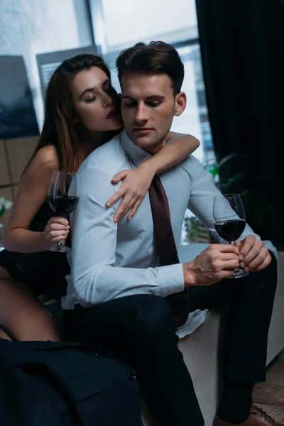 Petite amie embrasser homme d'affaires et tenant verre de vin dans l'appartement — Photo de stock