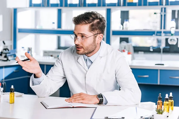 Schöner Arzt mit Brille gestikuliert, während er am Tisch sitzt — Stockfoto