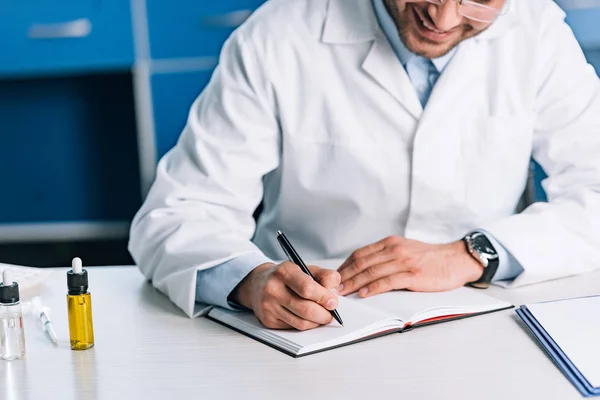 Ausgeschnittene Ansicht eines glücklichen Arztes, der in Notizbuch schreibt — Stockfoto