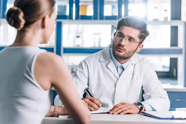 Selective focus of handsome doctor holding pen and looking at patient — Stock Photo