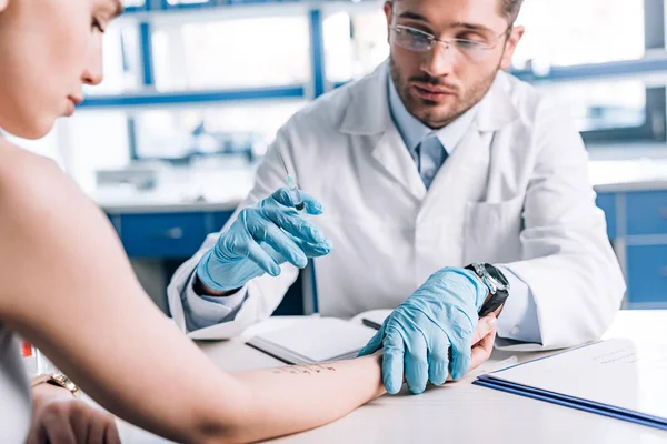 Foco seletivo do alergista em luvas de látex segurando seringa perto de mulher atraente na clínica — Fotografia de Stock
